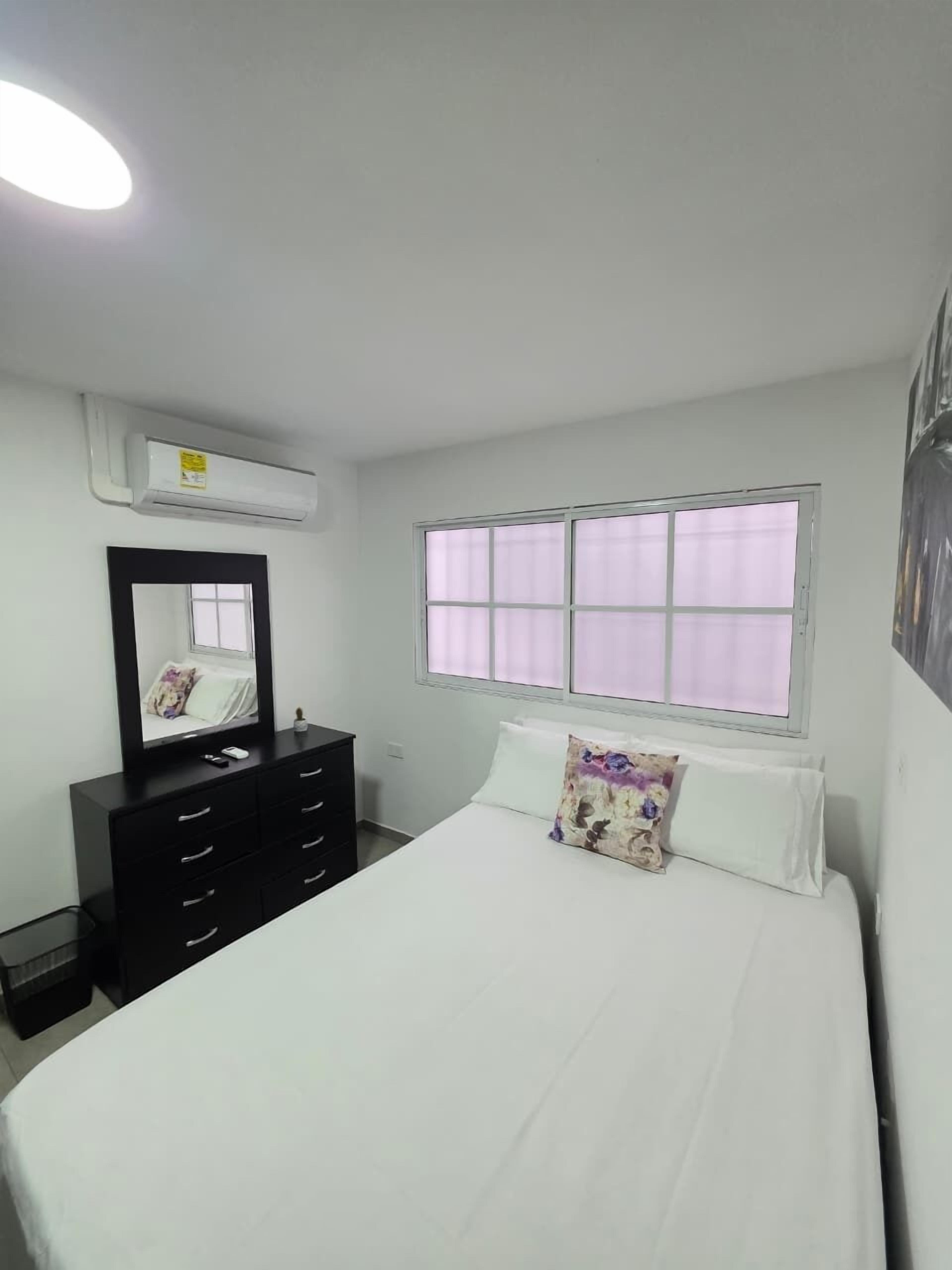A bedroom with a bed, a dresser, a mirror, and a window.