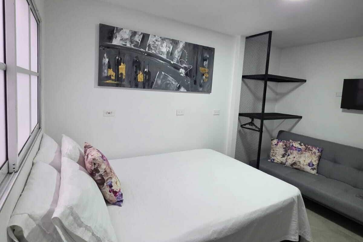 A modern bedroom with a bed, a sofa, a wall-mounted TV, and a painting.