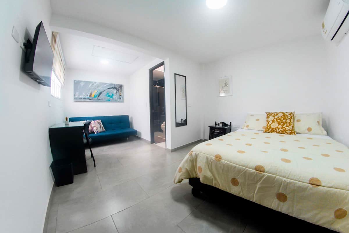 A bedroom with a bed, a blue sofa, a small table, and a TV mounted on the wall.