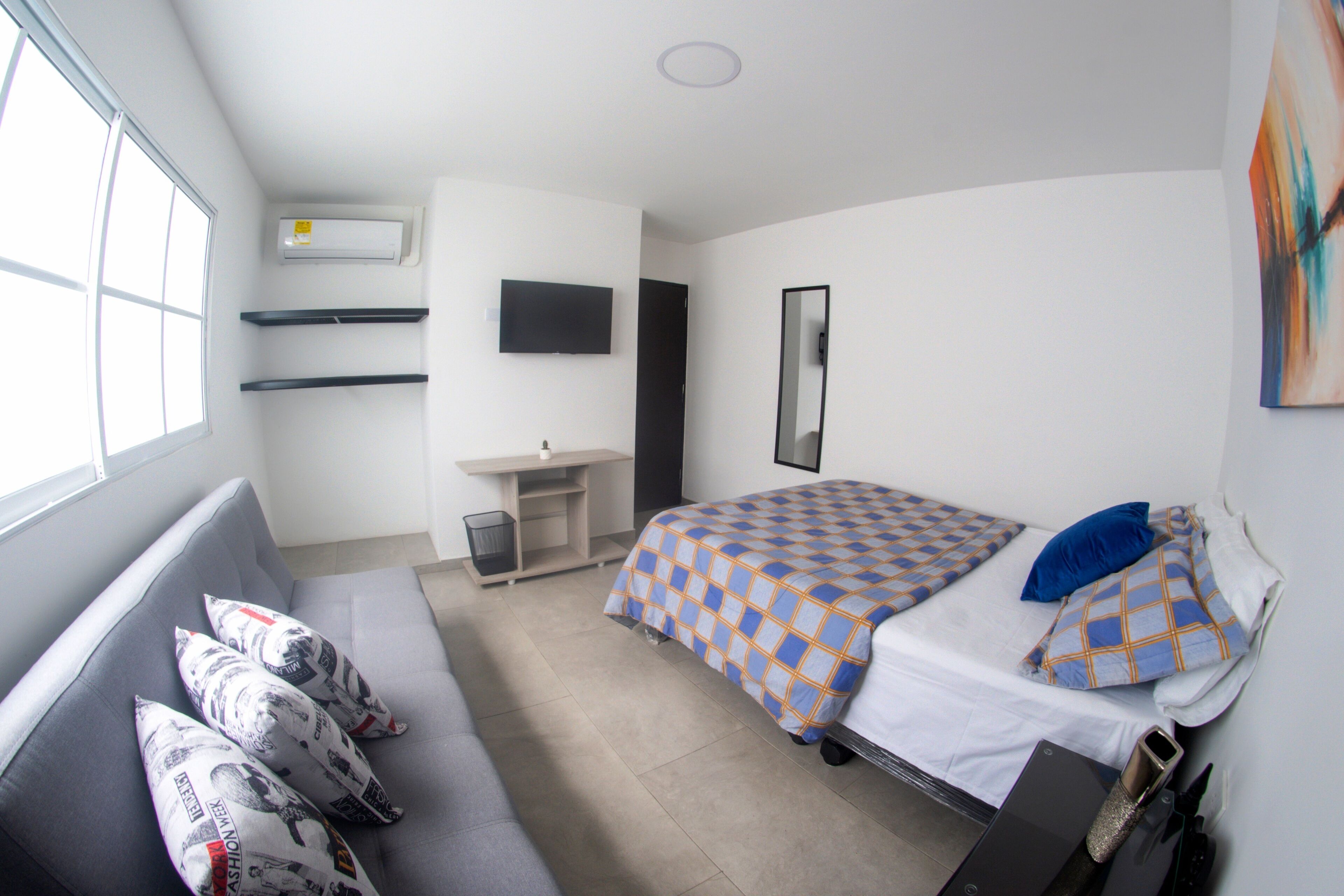 A bedroom with a bed, a desk, a chair, a window, and a wall-mounted TV.