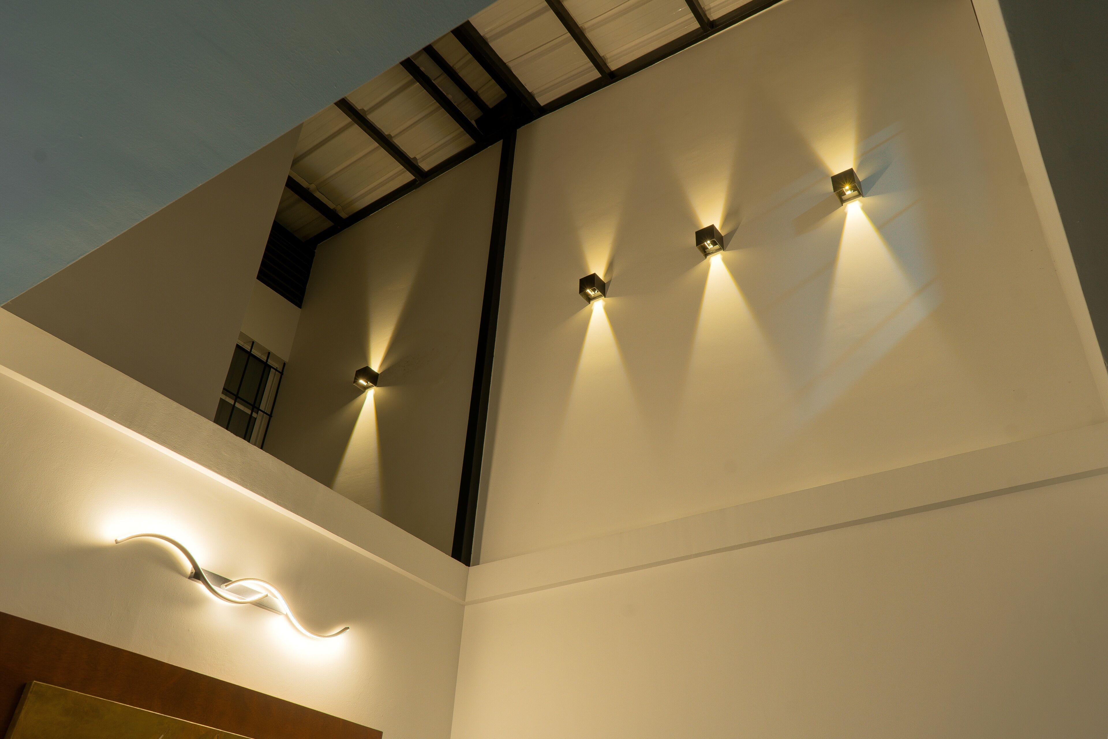 A modern interior with a sloped ceiling, recessed lighting, and a wavy light fixture.