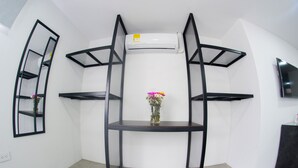 Une pièce d’angle avec une étagère en métal noir, un petit vase avec des fleurs et un téléviseur fixé au mur.