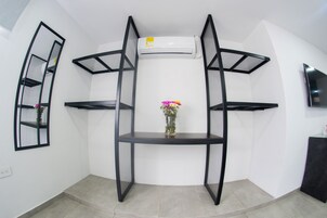 A corner room with a black metal shelf unit, a small vase with flowers, and a mounted TV.