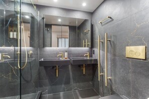 Ein modernes Badezimmer mit zwei Waschbecken, einer Duschkabine aus Glas und einem großen Spiegel.