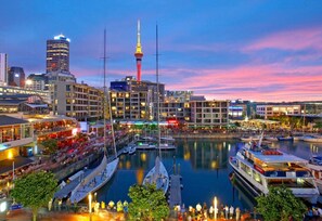 The Viaduct at night in full swing — restaurants glowing, the Sky Tower presiding over it all, and the energy of the city right outside. - Designer Harbour Stunner with Welcome Rosé (Auckland)