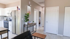 Een moderne keuken met witte kastjes, een roestvrijstalen koelkast en een eethoek met een zwarte stoel en een kleine tafel.