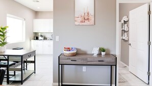 Een moderne keuken met witte kastjes, een eettafel en een klein bijzettafeltje met een plant en een mand met lekkernijen.