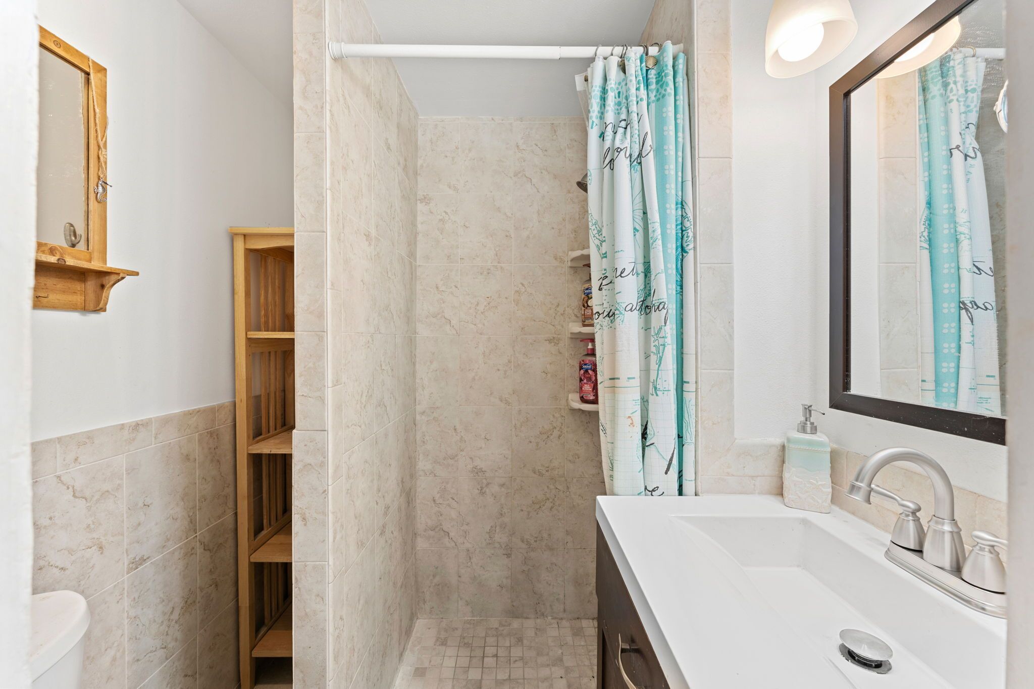 A bathroom with a shower, a sink, a mirror, and a wooden shelf.