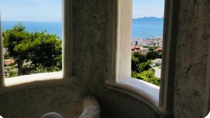 A view through a window with a curved frame, overlooking a coastal area with greenery and buildings. - Sumptuous Mediterranean villa in Cannes (Cannes)