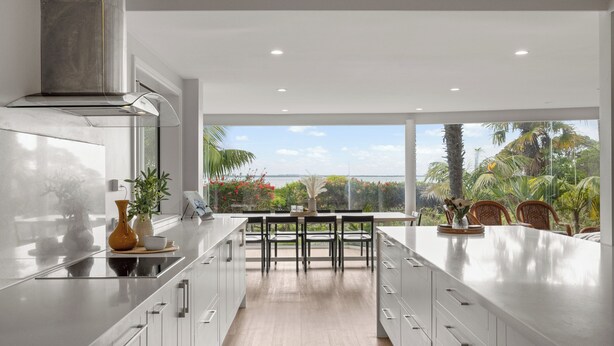 Cocina moderna con una isla grande, muebles blancos y vistas a un paisaje tropical.