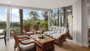 Una habitación amplia con un gran ventanal corredera que da a un jardín. En su interior, hay una mesa de centro de madera con sillas y un sofá.