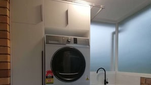 A compact kitchen with a built-in washer and dryer, a sink, and a window with a view. - Auckland Takapuna 2B Unit & Netflix (North shore)