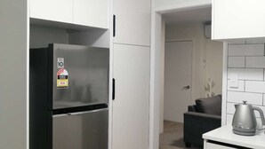 A compact kitchen with white cabinets, a stainless steel refrigerator, and a kettle on the countertop. - Auckland Takapuna 2B Unit & Netflix (North shore)