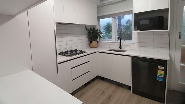 A modern kitchen with white cabinets, a gas stove, a sink, and a dishwasher. - Auckland Takapuna 2B Unit & Netflix (North shore)