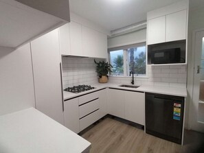 Moderni keittiö, jossa on valkoiset kaapit, kaasuliesi, pesuallas ja astianpesukone.