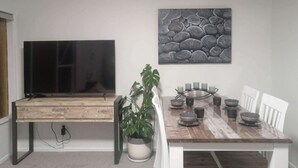 A dining area with a wooden table, chairs, a TV, and a painting on the wall. - Auckland Takapuna 2B Unit & Netflix (North shore)