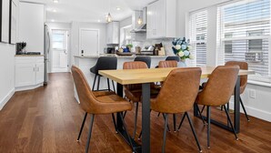 Een moderne keuken met witte kasten, een houten eettafel en zes bruine stoelen.