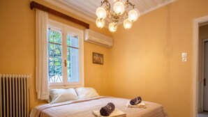 Une chambre à coucher comprenant un lit, un radiateur, un appareil de climatisation, une fenêtre avec des rideaux, un lustre et une porte.