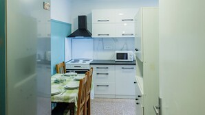 Une cuisine compacte avec des meubles blancs, un four à micro-ondes et une cuisinière. On y trouve une table à manger avec des chaises et un réfrigérateur.