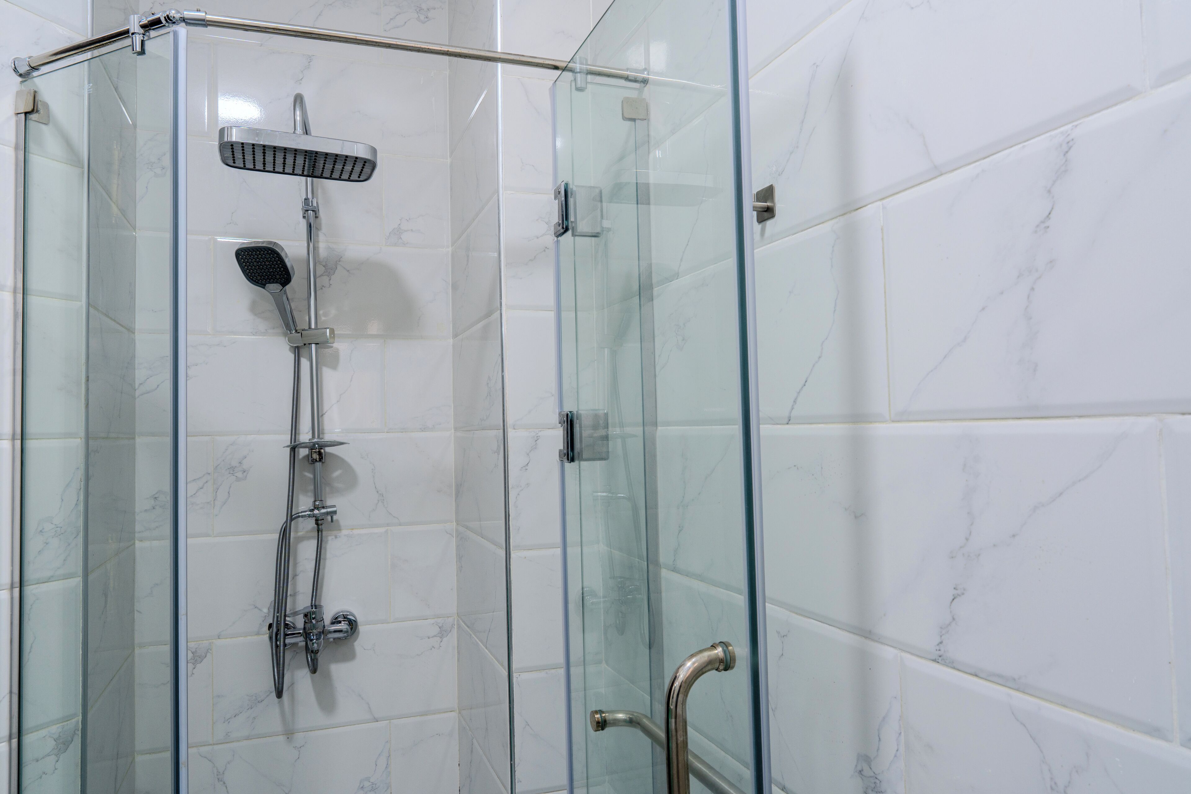 A glass-enclosed shower with a handheld showerhead and a wall-mounted faucet.
