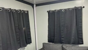 A room with a grey sofa, two black curtains, and a ceiling light. - TH2-Enjoy the serenity of the lake in the comfort of this 2 bedroom tiny home. (Bridgeport)