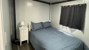 A bedroom with a bed, a nightstand, a lamp, and a window with curtains. - TH2-Enjoy the serenity of the lake in the comfort of this 2 bedroom tiny home. (Bridgeport)