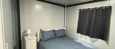 Un dormitorio con una cama, una mesita de noche, una lámpara y una ventana con cortinas.