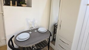 A compact room with a dining table, chairs, a clock, a wardrobe, and a window with curtains.