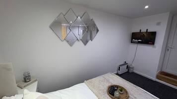 A hotel room with a bed, a wall-mounted TV, a small heater, and a decorative mirror.