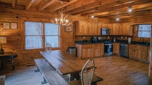 Ein Holzblockhaus-Interieur mit Esstisch, Bänken, einer Chandelüster, Holzausbau, einer Mikrowelle, einem Herd und einem Geschirrspüler.