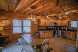 A wooden cabin interior with a dining table, benches, a chandelier, wooden cabinets, a microwave, stove, and dishwasher. - Cozy 3BR Log Cabin, 5 minutes to Center Hill Marina, Gated Community, Sleeps 10 (Lancaster)