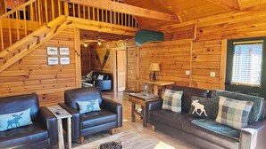 Ein gemütliches Blockhaus-Interieur mit Holzwänden, einer Treppe, Ledersofas und einem Esstisch.