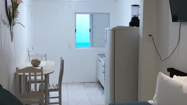 Une petite pièce comprenant un lit, un bureau avec une chaise, une fenêtre et un réfrigérateur.