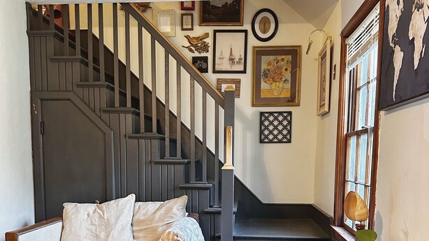 Un salón acogedor con una escalera de madera, un sofá, una mesa y varias fotografías enmarcadas en las paredes.