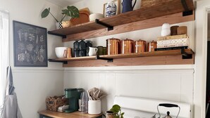 Una cocina con estantes de madera, un grabado botánico enmarcado y una estufa antigua.