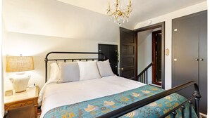 Un dormitorio con una cama, una mesita de noche, una lámpara, un candelabro y una puerta.