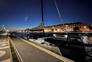 A nighttime waterfront scene with boats docked along a paved walkway, a building with illuminated windows in the background, and a clear sky. - HOME COMPIANI APARTMENT (Isola Sacra)