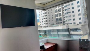 A room with a large window, a flat-screen TV mounted on the wall, a small wooden table, and a metal shelf. - Apartment in north downtown Quito, close to all parks and shopping centers. (Quito)