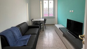 Un salon avec un canapé noir, un téléviseur et un coin repas comprenant une table et des chaises.