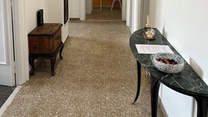 Un couloir avec une armoire en bois, une table en marbre sur laquelle se trouve un bol, et une chaise au fond.