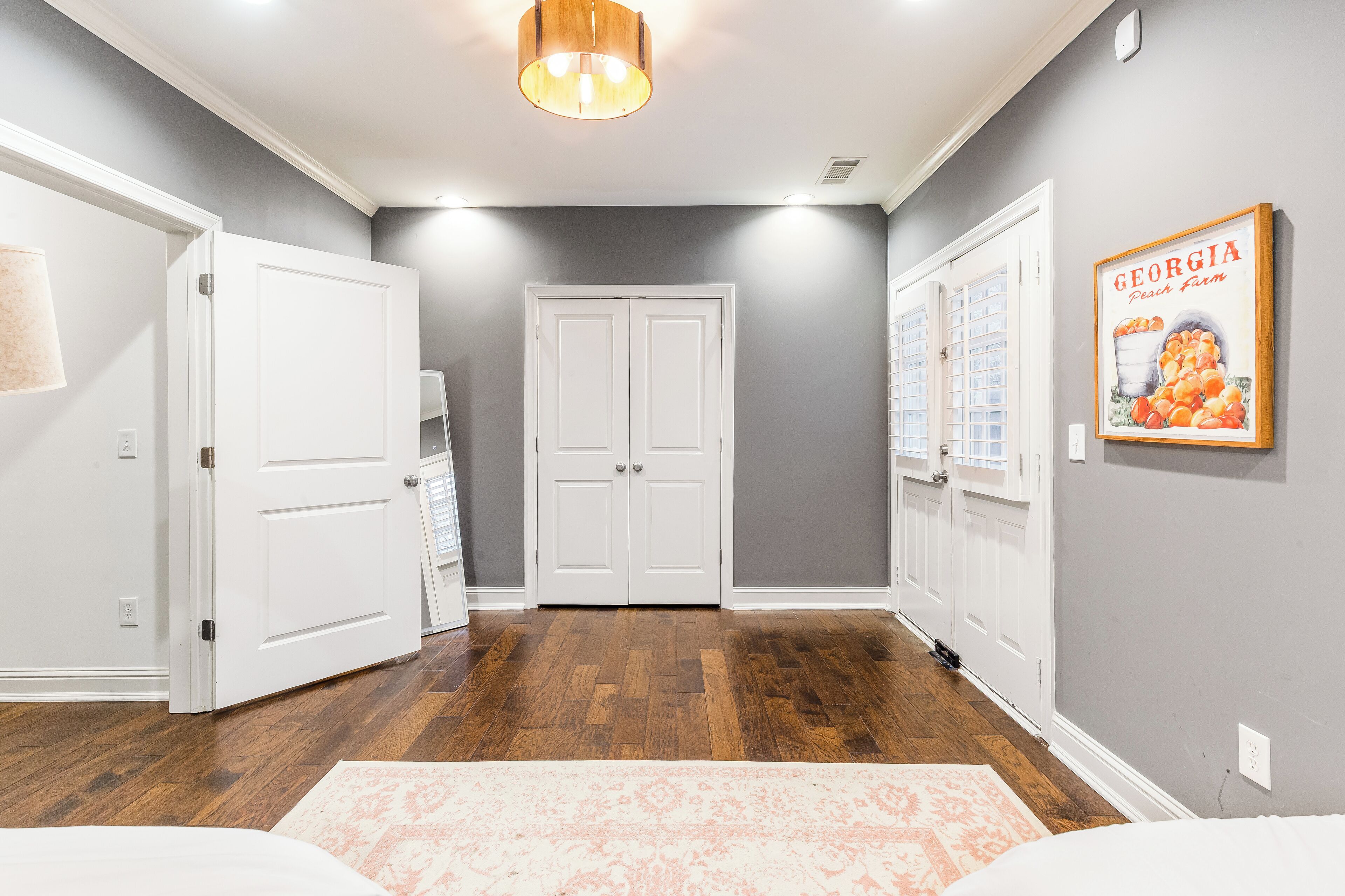 A hallway with hardwood flooring, white double doors, and a framed picture on the wall.