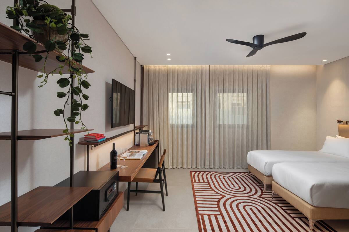 Een moderne hotelkamer met een bed, bureau en stoel, een plafondventilator en een groot raam met gordijnen.