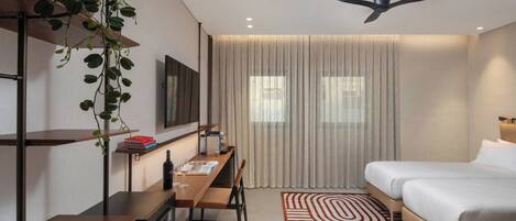 Una habitación de hotel moderna con cama, escritorio, silla, ventilador de techo y una ventana grande con cortinas.