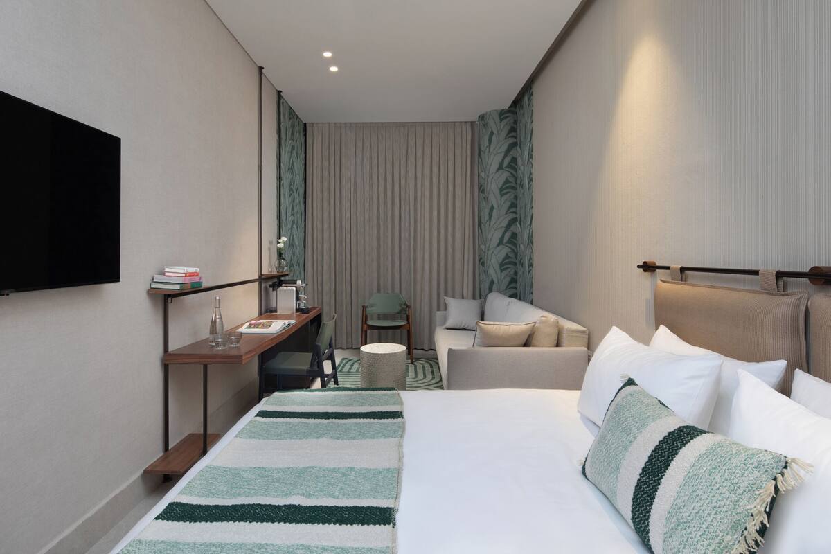 Een hotelkamer met een bed, bureau, stoel, televisie en raam met gordijnen.