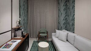 Een knus woongedeelte met een bank, een fauteuil, een koffieapparaat en een kleine tafel met een boek en een vaas.