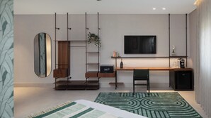 Een moderne woonkamer met een plafondventilator, een aan de muur bevestigde televisie, een houten bureau, een stoel en een kamerkleed met een patroon.