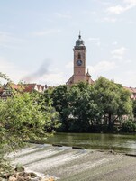 Um edifício histórico com uma torre de relógio, rodeado por árvores e um rio.