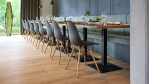 Un espace de salle à manger moderne, avec une longue table, de nombreuses chaises et des luminaires suspendus.