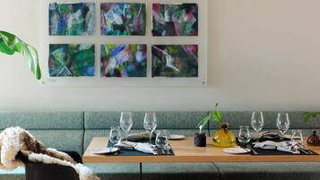 Een eethoek met een houten tafel gedekt voor vier personen, een groene bank en abstracte kunst aan de muur.