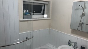 A bathroom with a bathtub, a sink, a window with a shelf, and a mirror. - Comfortable Room in a shared apartment. (Cardiff)